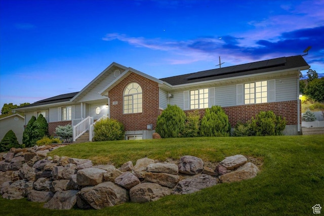 single story home featuring roof mounted solar panels, a lawn, and brick siding