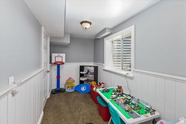 playroom featuring carpet floors, a wainscoted wall, and a textured ceiling