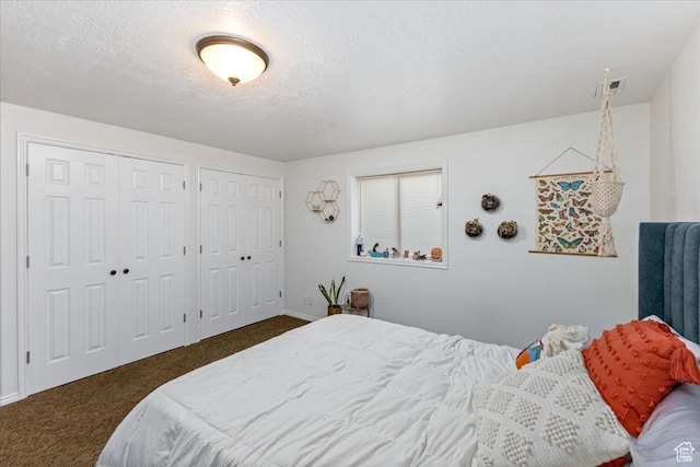 bedroom with a textured ceiling, dark colored carpet, and multiple closets