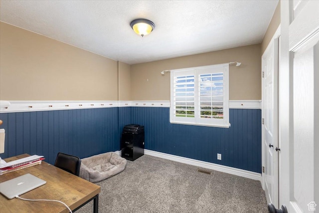 unfurnished office with a textured ceiling, carpet, visible vents, and a wainscoted wall