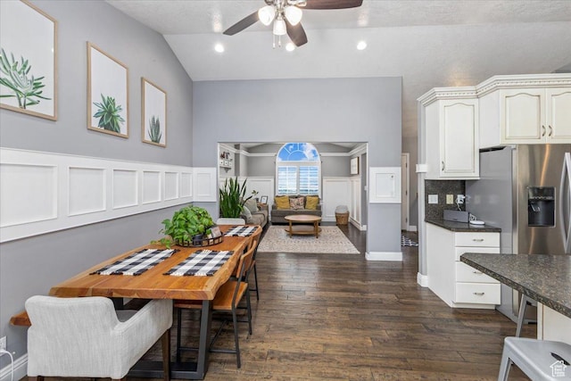 dining room with dark wood-type flooring, wainscoting, lofted ceiling, and ceiling fan