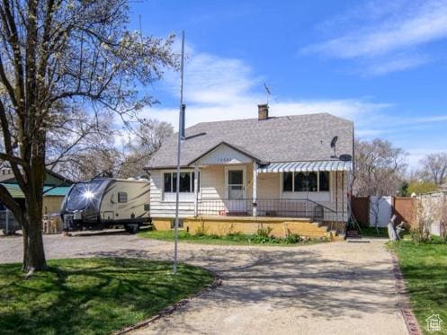 bungalow with a porch, a chimney, a front lawn, and dirt driveway