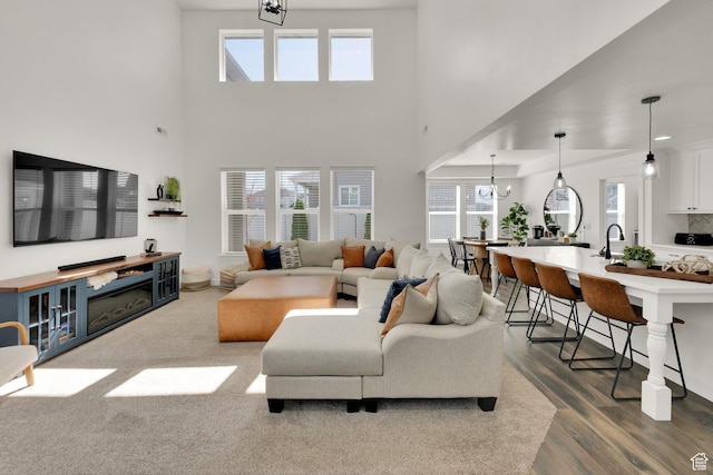 living room featuring plenty of natural light, a towering ceiling, an inviting chandelier, and wood finished floors
