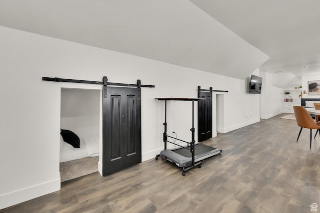 workout room featuring baseboards, a barn door, wood finished floors, and lofted ceiling