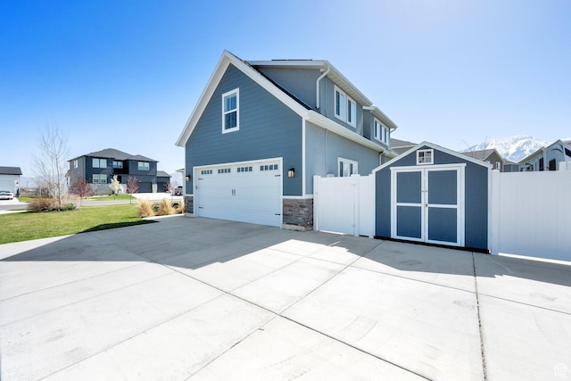 view of home's exterior featuring concrete driveway, stone siding, a garage, fence, and a storage unit