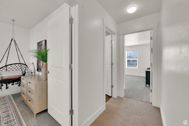 hall featuring light colored carpet and baseboards