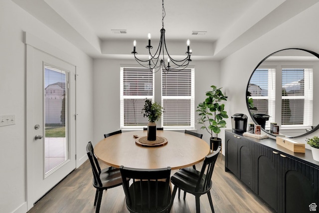 dining room with a chandelier, light wood finished floors, visible vents, and a tray ceiling