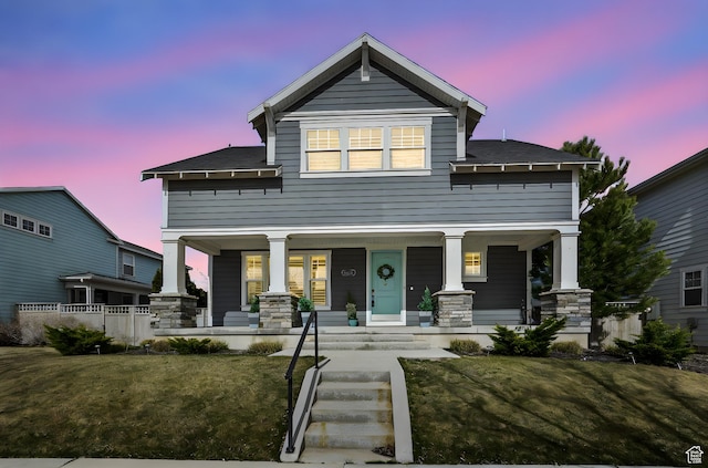 view of front facade with a porch, roof with shingles, stone siding, and a front lawn