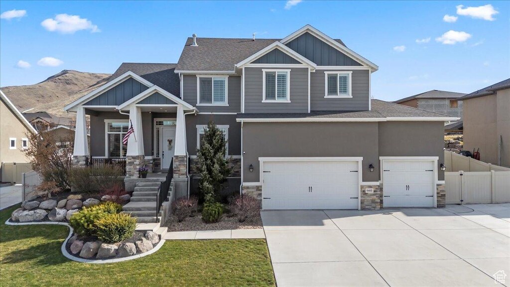 craftsman-style home with concrete driveway, stone siding, board and batten siding, an attached garage, and fence