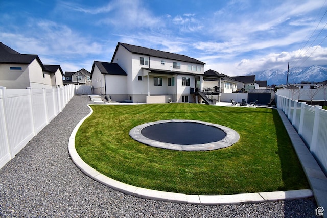 rear view of house featuring a fenced backyard, a trampoline, a residential view, and stucco siding