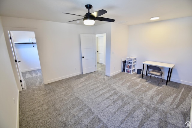 unfurnished bedroom with a walk in closet, carpet, baseboards, and ceiling fan