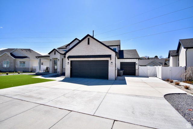modern farmhouse style home with a gate, fence, brick siding, an attached garage, and concrete driveway