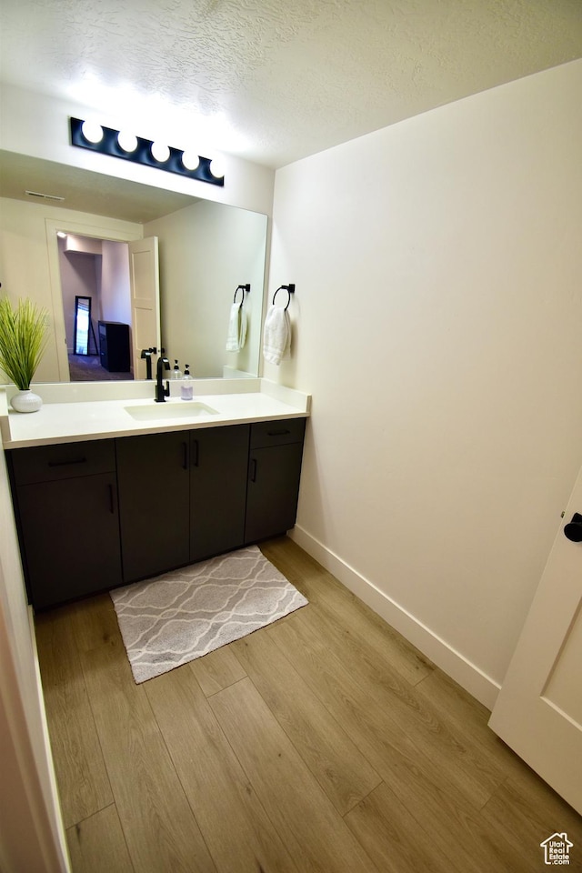 bathroom featuring baseboards, vanity, wood finished floors, and a textured ceiling