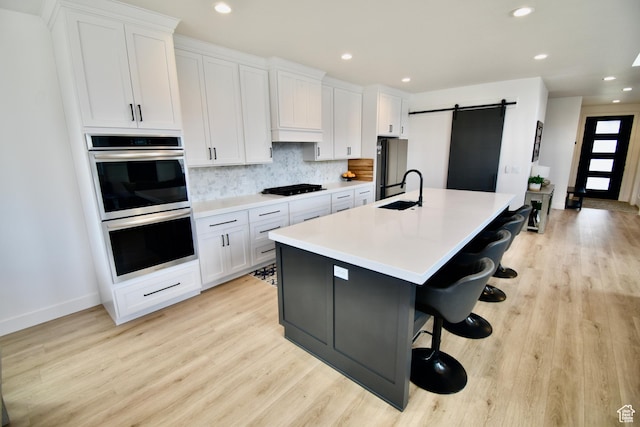kitchen featuring tasteful backsplash, white cabinets, a barn door, stainless steel appliances, and a center island with sink
