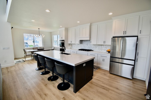 kitchen with a sink, black stovetop, light countertops, freestanding refrigerator, and a center island with sink