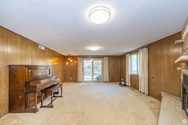 sitting room featuring wooden walls, visible vents, light colored carpet, and a fireplace
