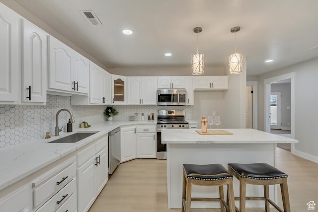 kitchen with a sink, appliances with stainless steel finishes, white cabinetry, backsplash, and a breakfast bar area