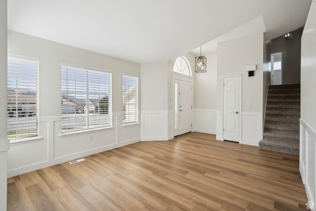 unfurnished dining area featuring light wood-type flooring, wainscoting, visible vents, and stairs