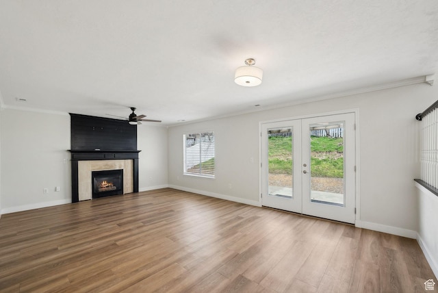 unfurnished living room featuring ceiling fan, ornamental molding, wood finished floors, a tile fireplace, and baseboards