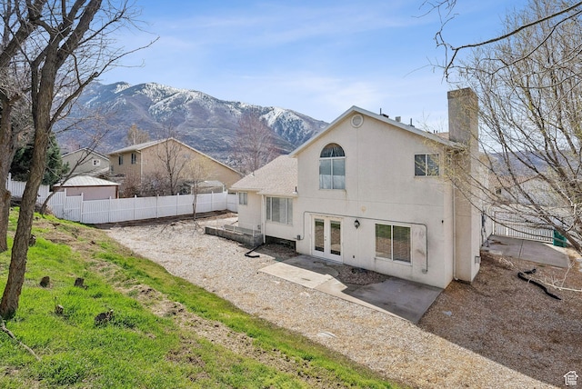 back of property with stucco siding, a mountain view, a chimney, french doors, and fence