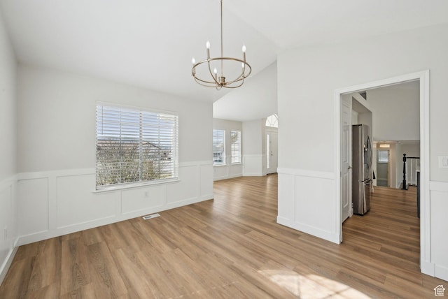 unfurnished dining area featuring light wood-type flooring, visible vents, a chandelier, wainscoting, and lofted ceiling
