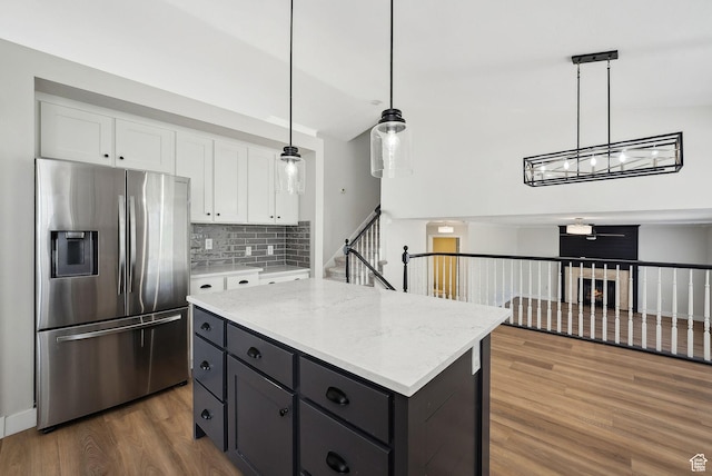 kitchen with stainless steel refrigerator with ice dispenser, white cabinetry, wood finished floors, decorative backsplash, and a kitchen island