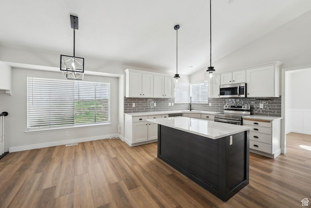 kitchen with white cabinets, a sink, light countertops, vaulted ceiling, and stainless steel appliances