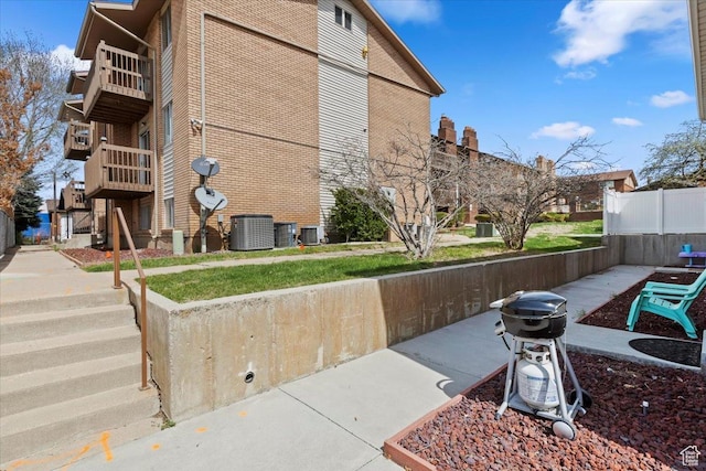 exterior space with a balcony, brick siding, fence, and central AC