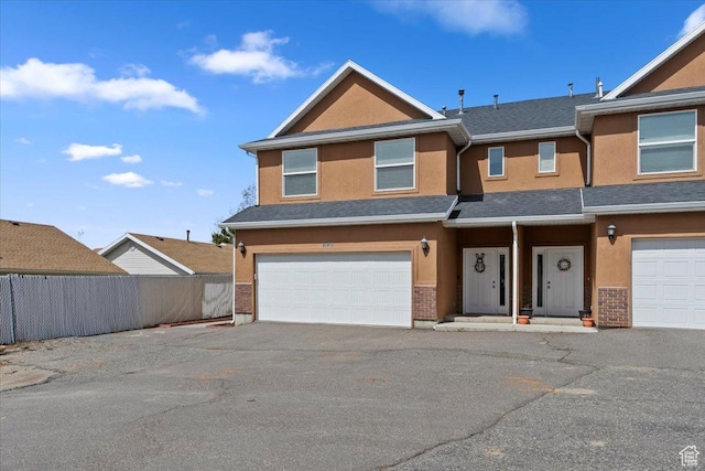 view of front of house with an attached garage, fence, aphalt driveway, and stucco siding
