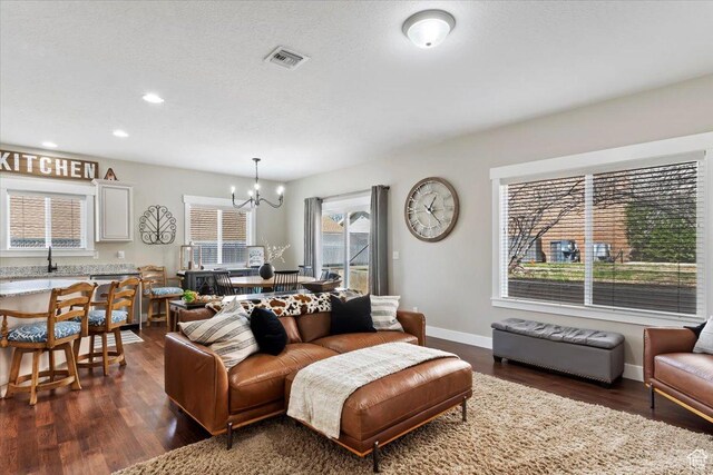 living room featuring a chandelier, dark wood-type flooring, visible vents, and baseboards