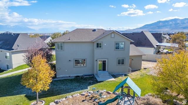 rear view of property with a mountain view, entry steps, a lawn, fence, and stucco siding