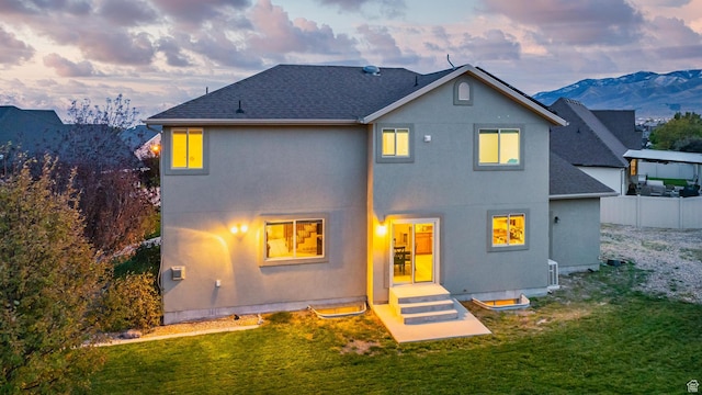back of property at dusk featuring a yard, fence, stucco siding, and roof with shingles