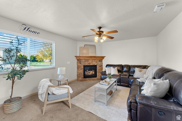 living area featuring a textured ceiling, light colored carpet, a ceiling fan, and a stone fireplace