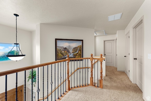 hallway with an upstairs landing, visible vents, a textured ceiling, and carpet floors