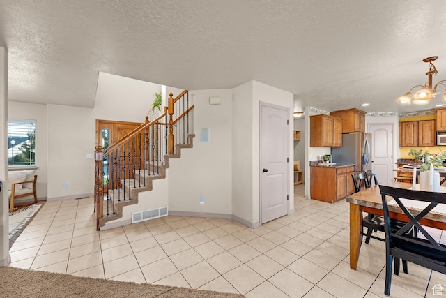 interior space with visible vents, light tile patterned floors, a chandelier, a textured ceiling, and stairway