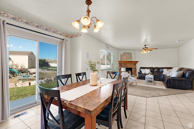 dining area with visible vents, a lit fireplace, ceiling fan with notable chandelier, and light tile patterned flooring