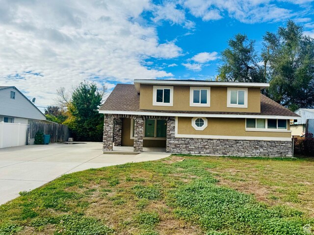 view of front facade featuring stone siding, stucco siding, fence, and a front yard