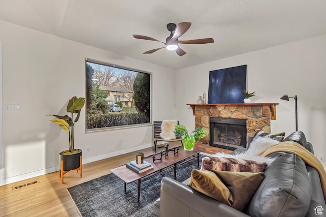 living area featuring visible vents, baseboards, a stone fireplace, a ceiling fan, and wood finished floors