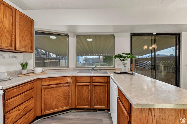 kitchen with brown cabinetry, a peninsula, light countertops, a sink, and plenty of natural light