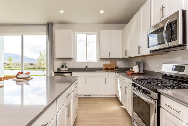 kitchen with white cabinets, light wood-style flooring, a sink, and appliances with stainless steel finishes