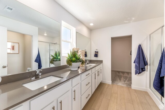 full bathroom with a sink, a shower stall, double vanity, and wood finished floors