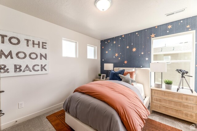 carpeted bedroom featuring visible vents, baseboards, wallpapered walls, and an accent wall