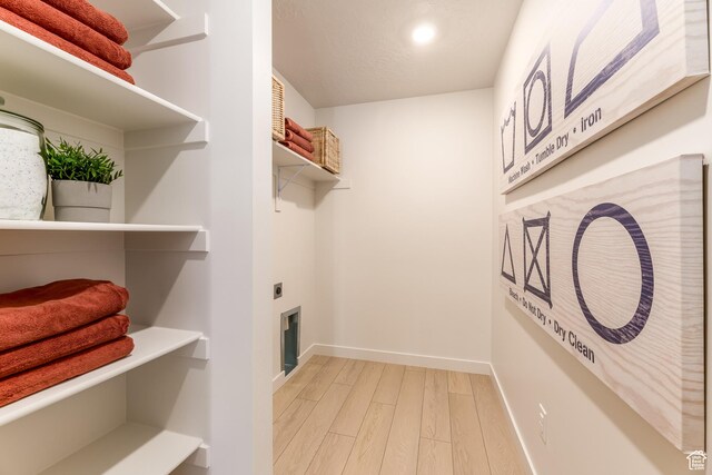 clothes washing area featuring hookup for an electric dryer, light wood-style flooring, laundry area, and baseboards