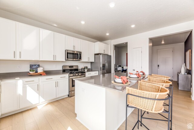 kitchen featuring a breakfast bar, light wood-type flooring, a center island, white cabinetry, and appliances with stainless steel finishes