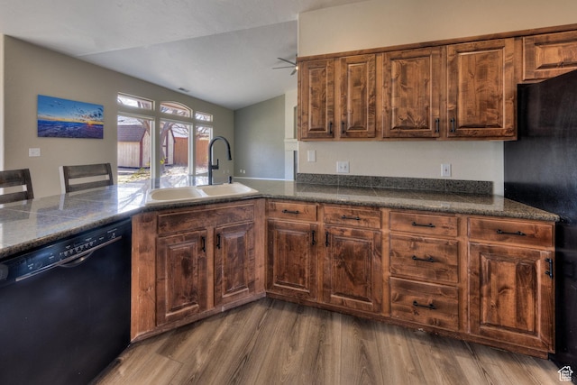 kitchen with black appliances, wood finished floors, a sink, dark countertops, and lofted ceiling