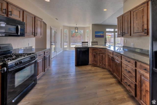 kitchen with dark wood-style flooring, recessed lighting, a peninsula, black appliances, and a sink