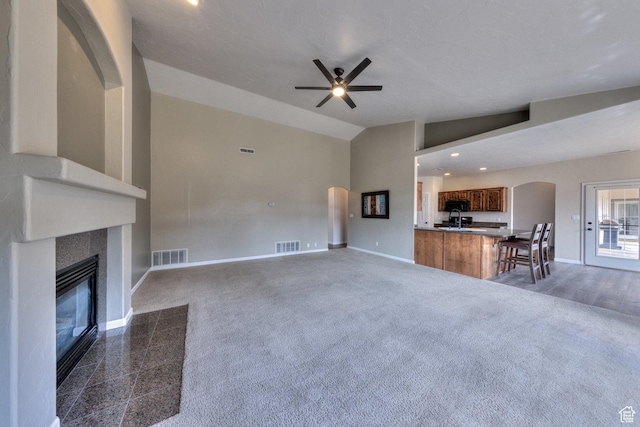 unfurnished living room featuring vaulted ceiling, a tiled fireplace, visible vents, ceiling fan, and arched walkways