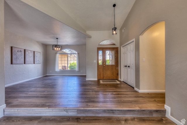 entryway with arched walkways, wood finished floors, an inviting chandelier, and baseboards