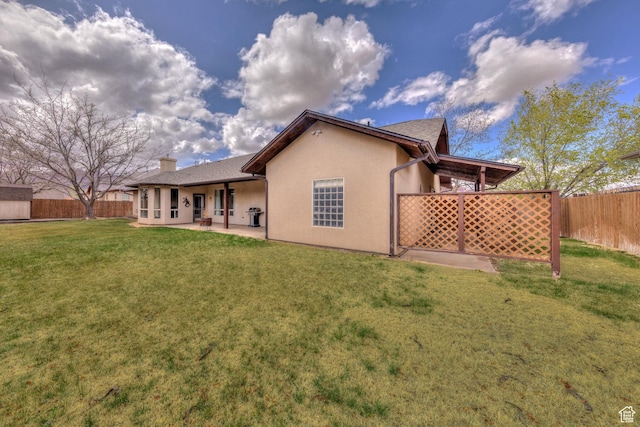 rear view of house with a yard, a chimney, a fenced backyard, a patio, and stucco siding