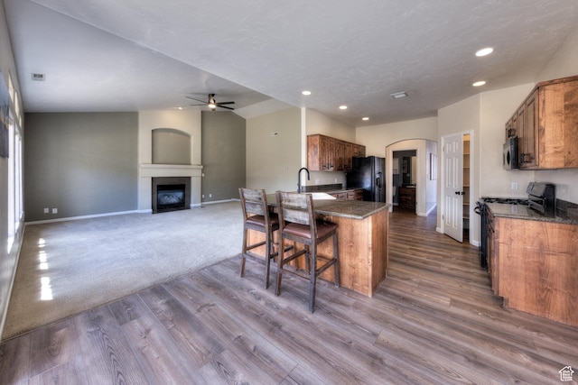 kitchen featuring ceiling fan, black refrigerator with ice dispenser, stainless steel microwave, range with gas stovetop, and brown cabinets